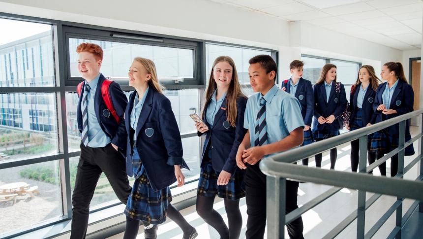 Secondary school class walking down hall to classroom talking.