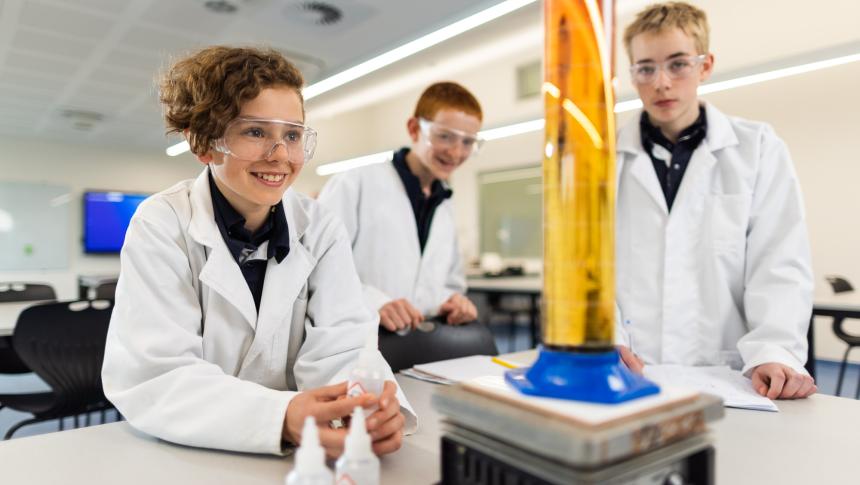 Students in lab coats and safety goggles working in science lab.