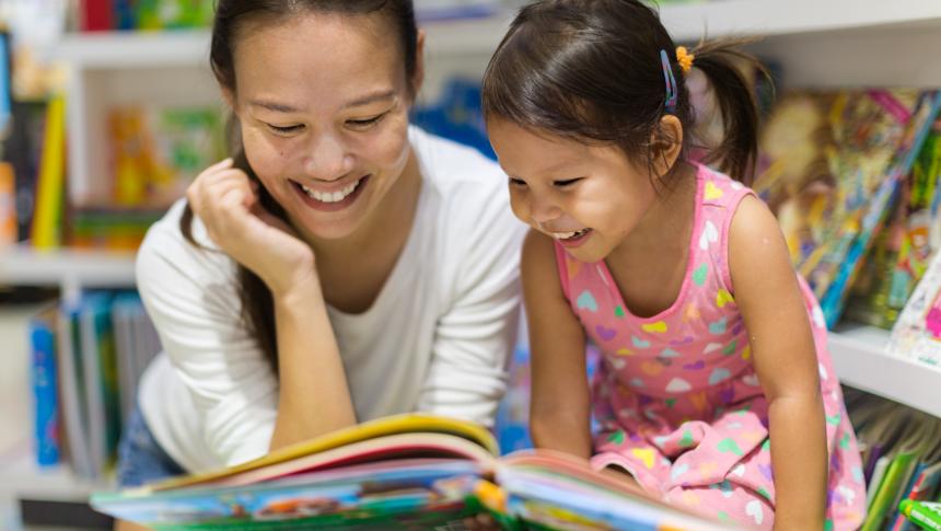 Smiling early childhood teacher or educator and child reading picture book together.