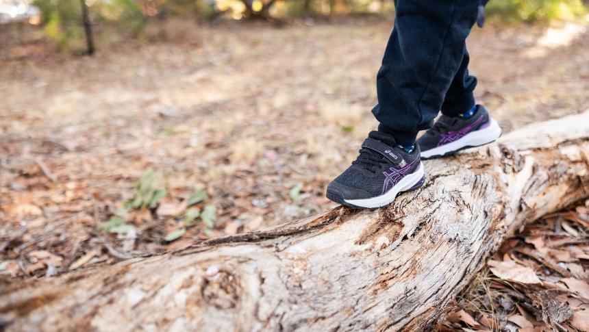 Child's feet shown balancing on a log outdoors.