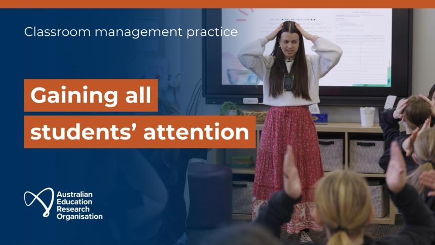 A teacher stands in front of a class of students of students with her hands on her head. 