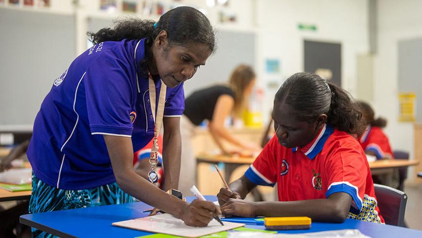 Teacher leaning over students desk giving feedback on writing