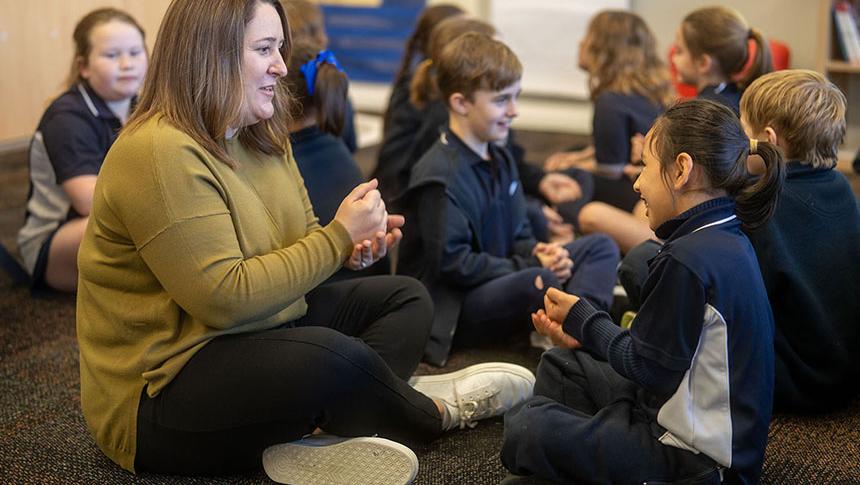 Teacher sitting on floor with students performing actions with hands