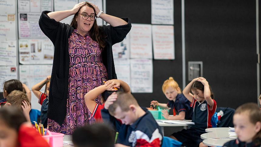 Teacher putting hands on head to gets students attention while students copy the action