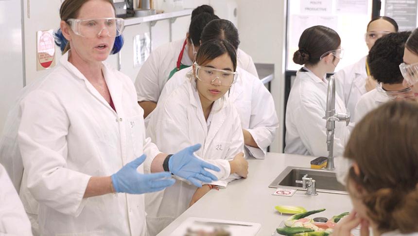 Teacher talking to students at lab table while demonstrating dissecting a frog