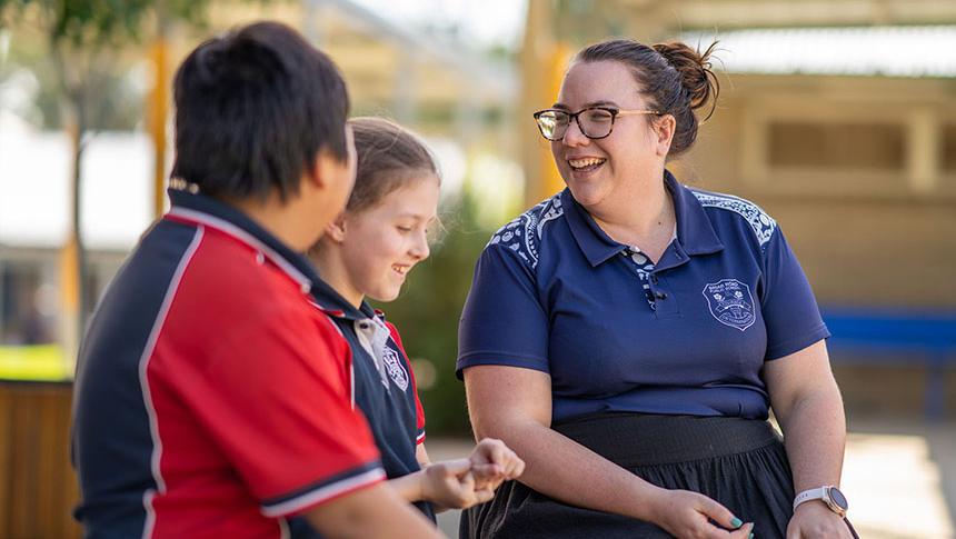 Teacher talking to 2 students on bench outside classroom