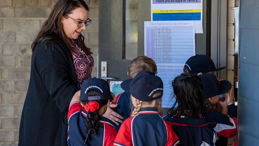 Teacher greeting students lining up at door as they enter the classroom