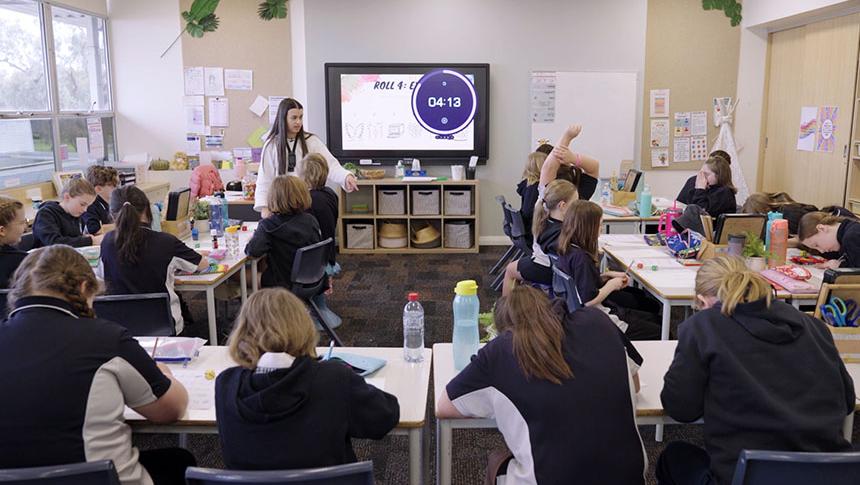 Class working at desks while teacher responds to student with their hand up