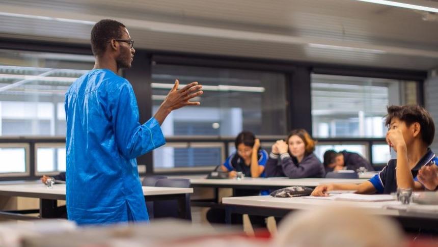 Teacher standing at front of classroom talking to students sitting at their desks