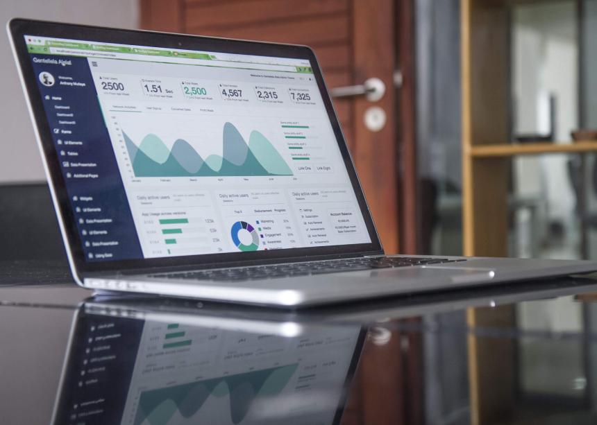 A laptop sits open on a mirror-topped desk. On the screen are a number of charts and graphs. The words and numbers are not legible but look like a school improvement dashboard.