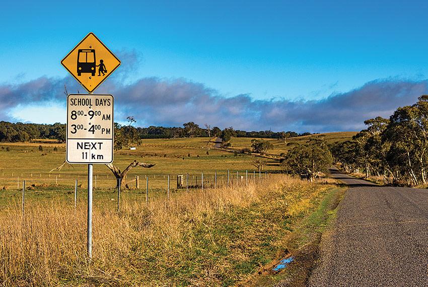 A photograph of an Australian country road and landscape, with a road sign indicating school bus times. 