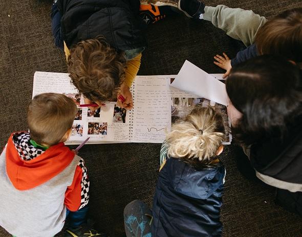 A view from above of children in a early learning setting on the floor looking at a handwritten book with images. 