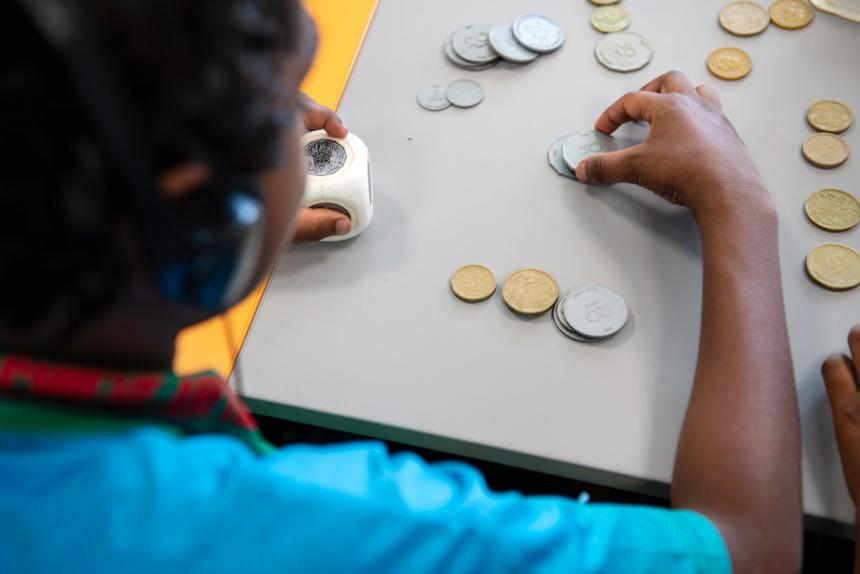 A photograph from behind of a young boy counting plastic coins. 