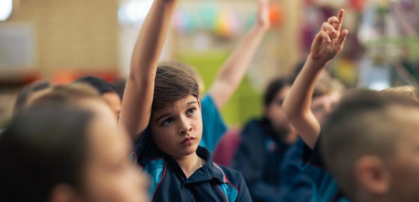 A group of children in a classroom with their hands up