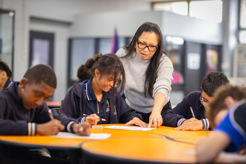 Secondary school teacher leaning over group table, giving students feedback.