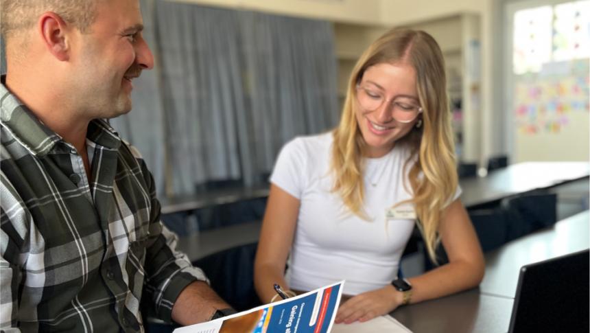 Two smiling school staff members work together at a desk in a classroom